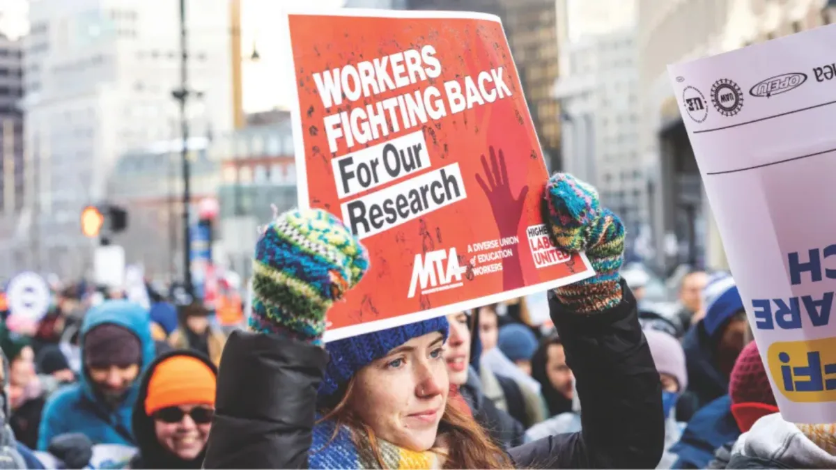 Protester holding a sign with "Workers Fight Back for Our Research" at a rally held in 2025 against the Trump administration's efforts to reduce federal research dollars to higher education.