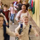 A group of nine elementary-school-aged students running through the hallway of a school