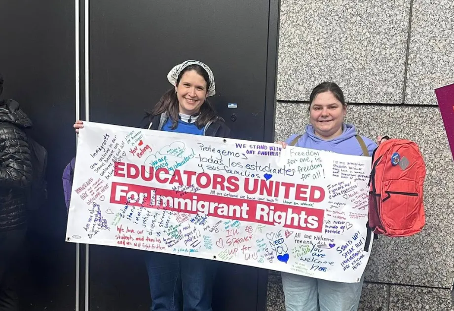 Two women are holding a banner that reads: Educators United for Immigrant Rights. The photo was taken at a Safe Schools action held immediately following the MTA Annual Meeting of Delegates on Saturday, May 9, 2026.