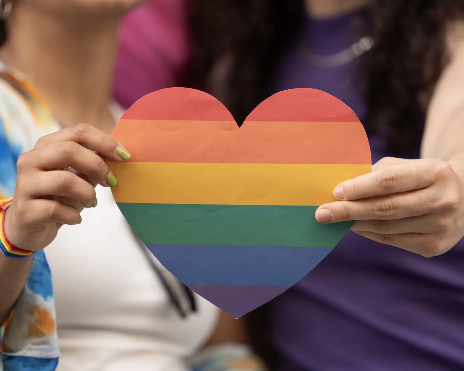Hands holding a cutout of a heart in pride colors