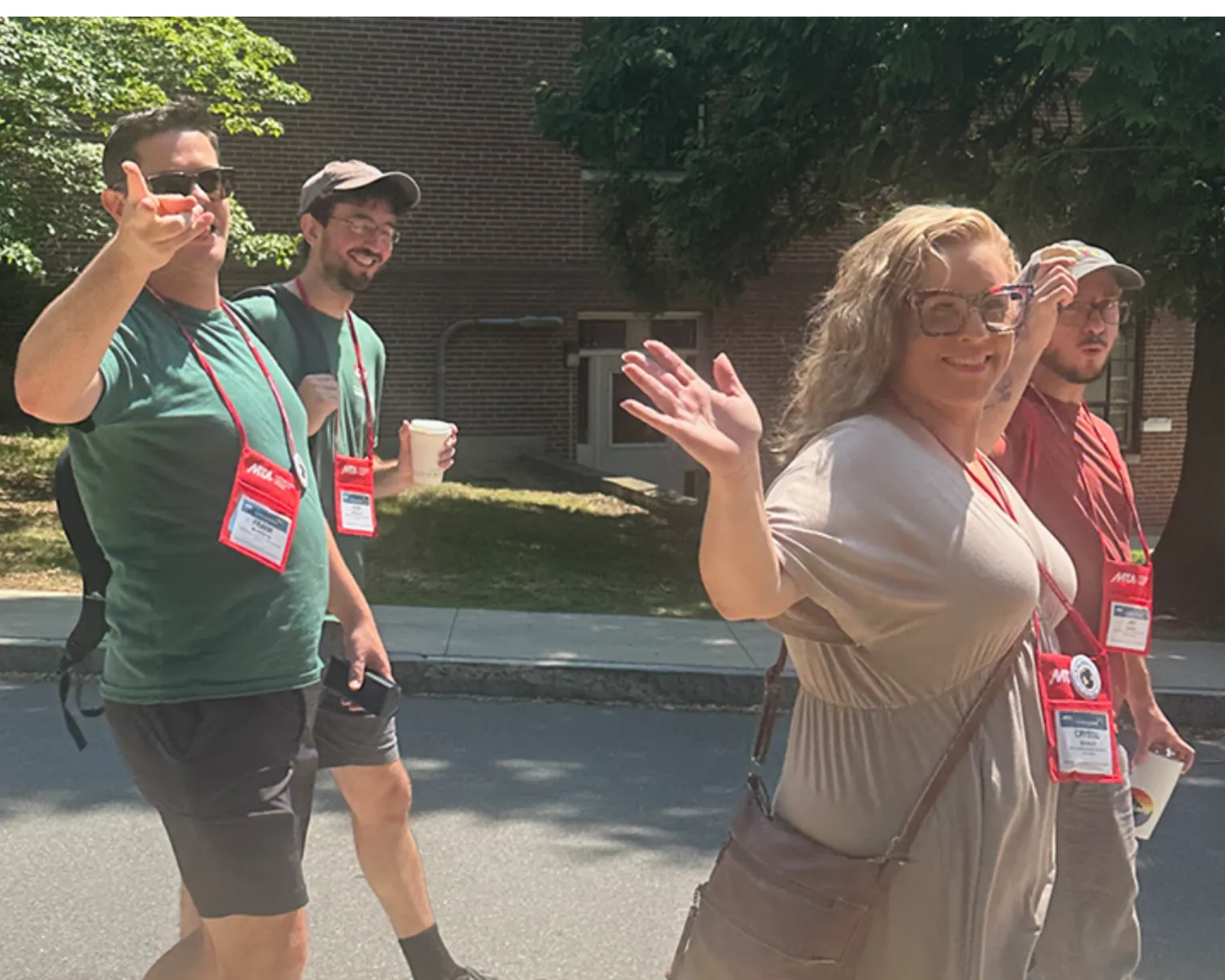 Three men and two woman are giving the thumbs up as they walk on the campus of UMass Amherst, where they are participating in the Summer Conference.