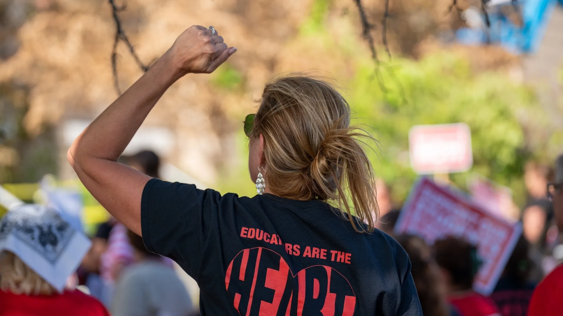 Educator raising a fist, wearing a T-shirt that says “Educators Are the Heart”