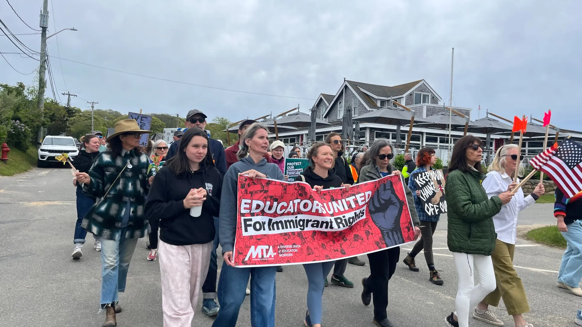 May 23 2026 Rally on Martha's Vineyard in support of a student and his father who were taken by ICE. At the forefront are three teachers carrying a banner that says "Educators United for Immigrant Rights" with the MTA logo. There are also several other people walking with them, including many students.