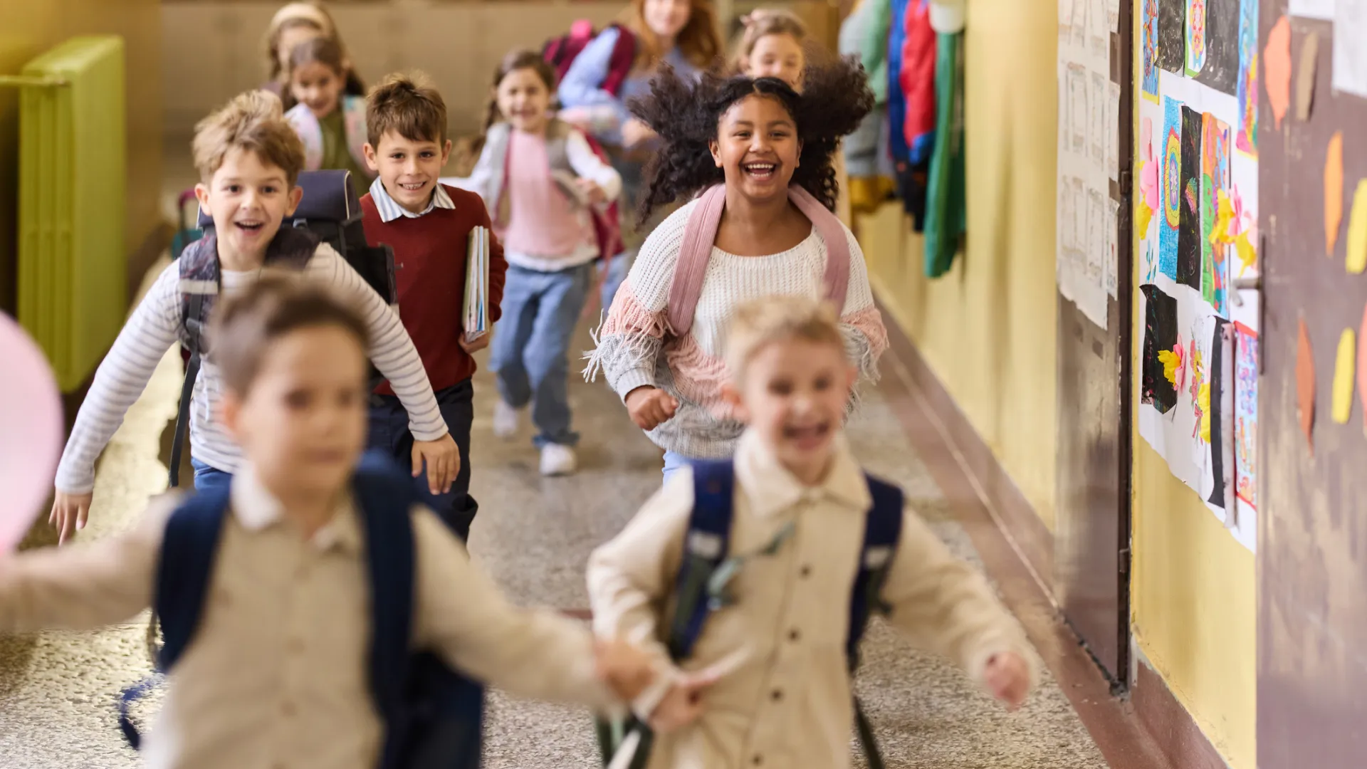 A group of nine elementary-school-aged students running through the hallway of a school