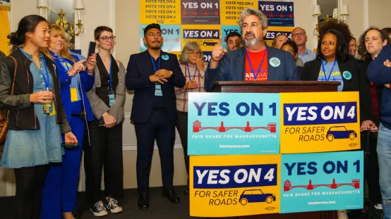 Max Page speaking at a press conference celebrating the victory of the Massachusetts Fair Share Amendment (“Yes on 1”).