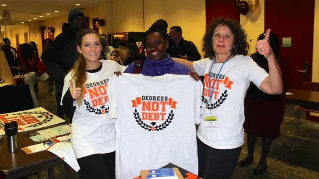 Two student teachers and a union staff-person stand with t-shirts that read "Degrees Not Debt."