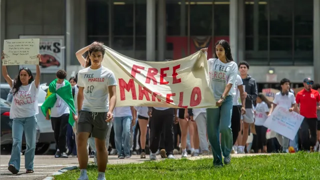 Teenagers walking in a high school holding a sign that says “Free Marcelo.”