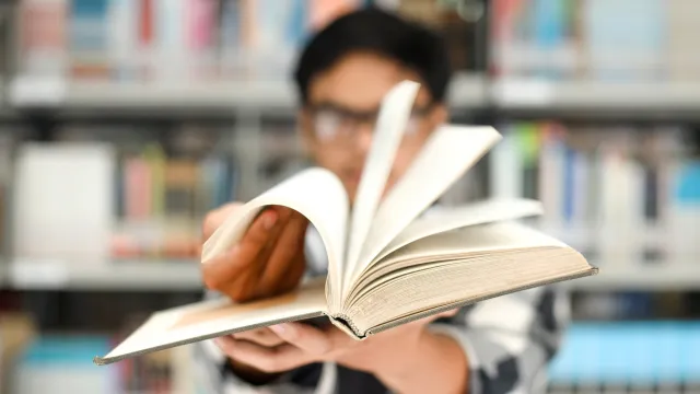 Educator flipping through a book with a bookshelf in the background