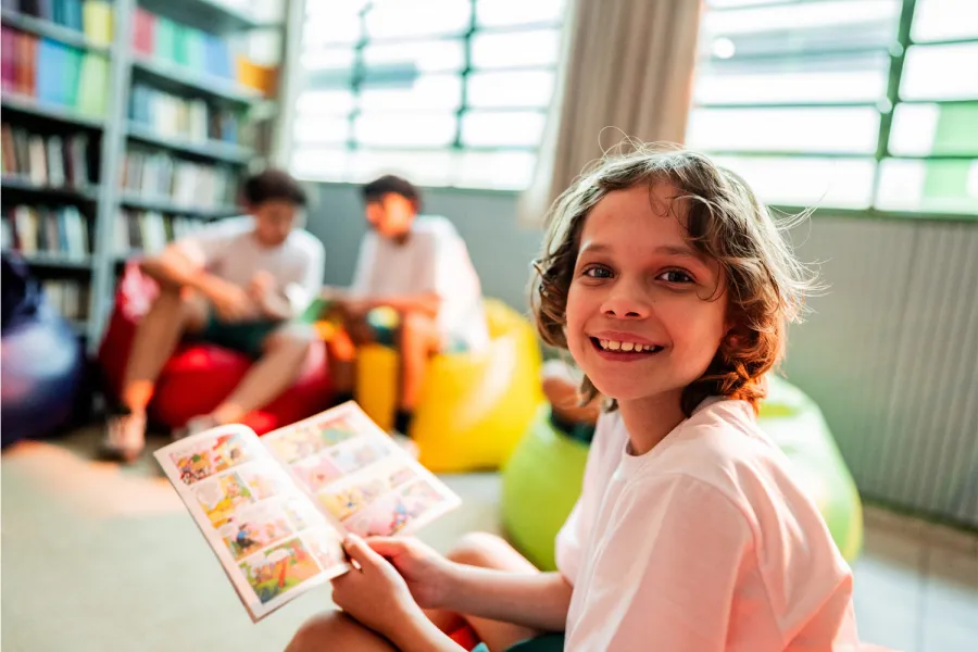 A young reader absorbed in a book among the quiet shelves of a library.